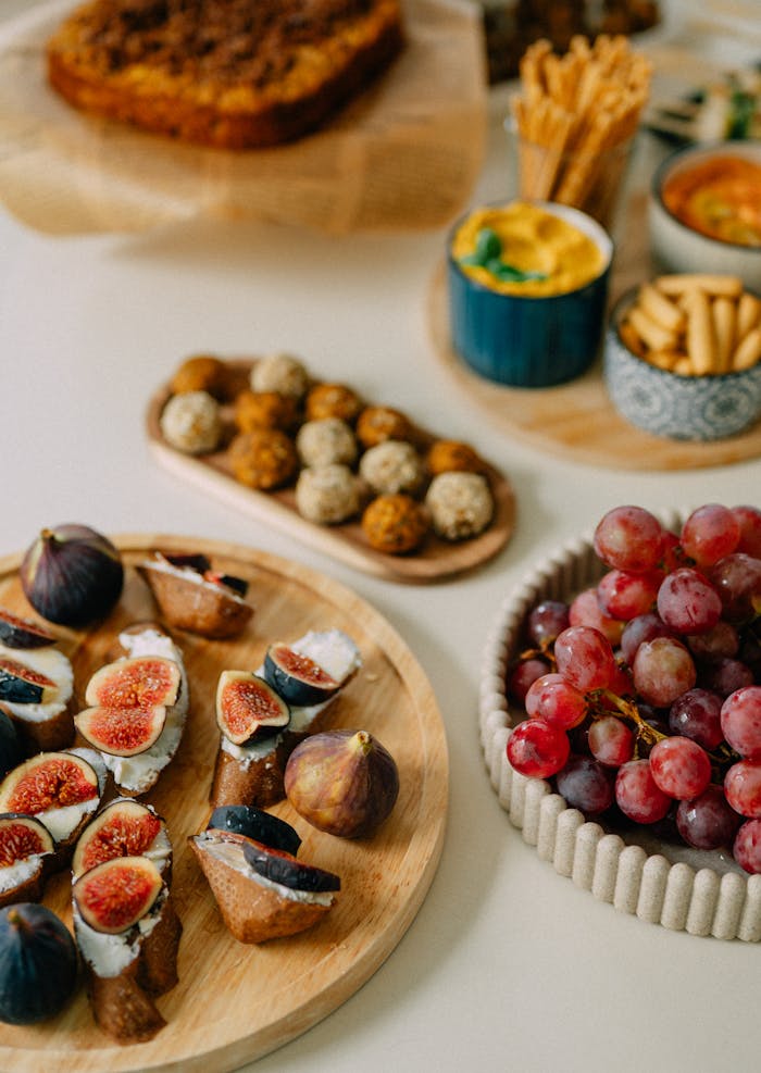 A beautifully arranged platter featuring figs, grapes, and mixed appetizers on a wooden tray.
