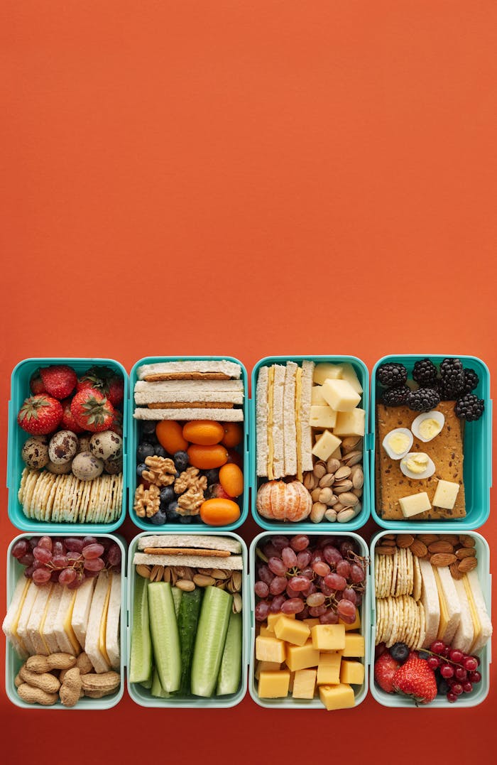 Top view of diverse snack boxes arranged neatly on an orange backdrop, ideal for meal prep inspiration.